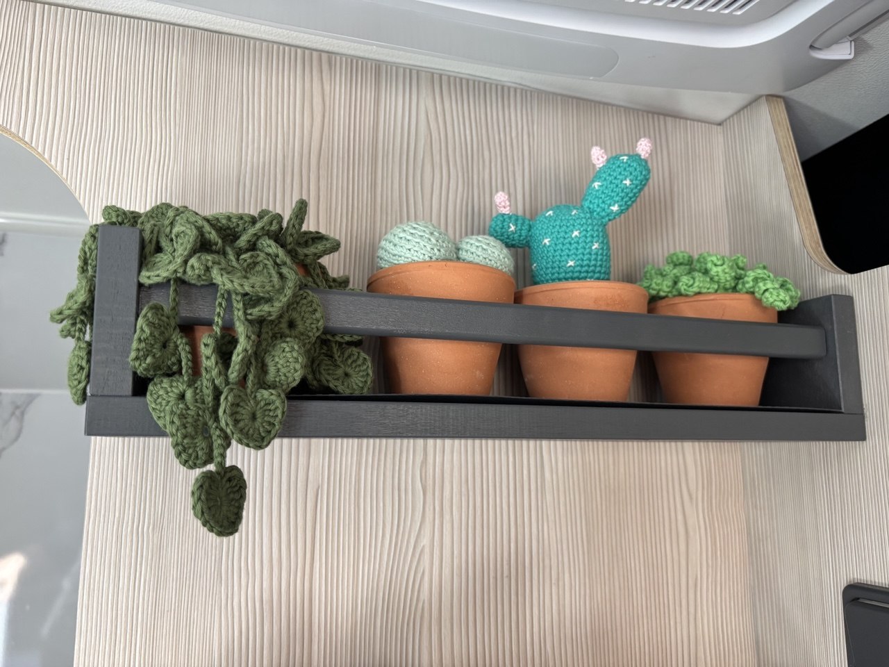 Estantería negra con plantas y cactus de ganchillo sobre la madera clara